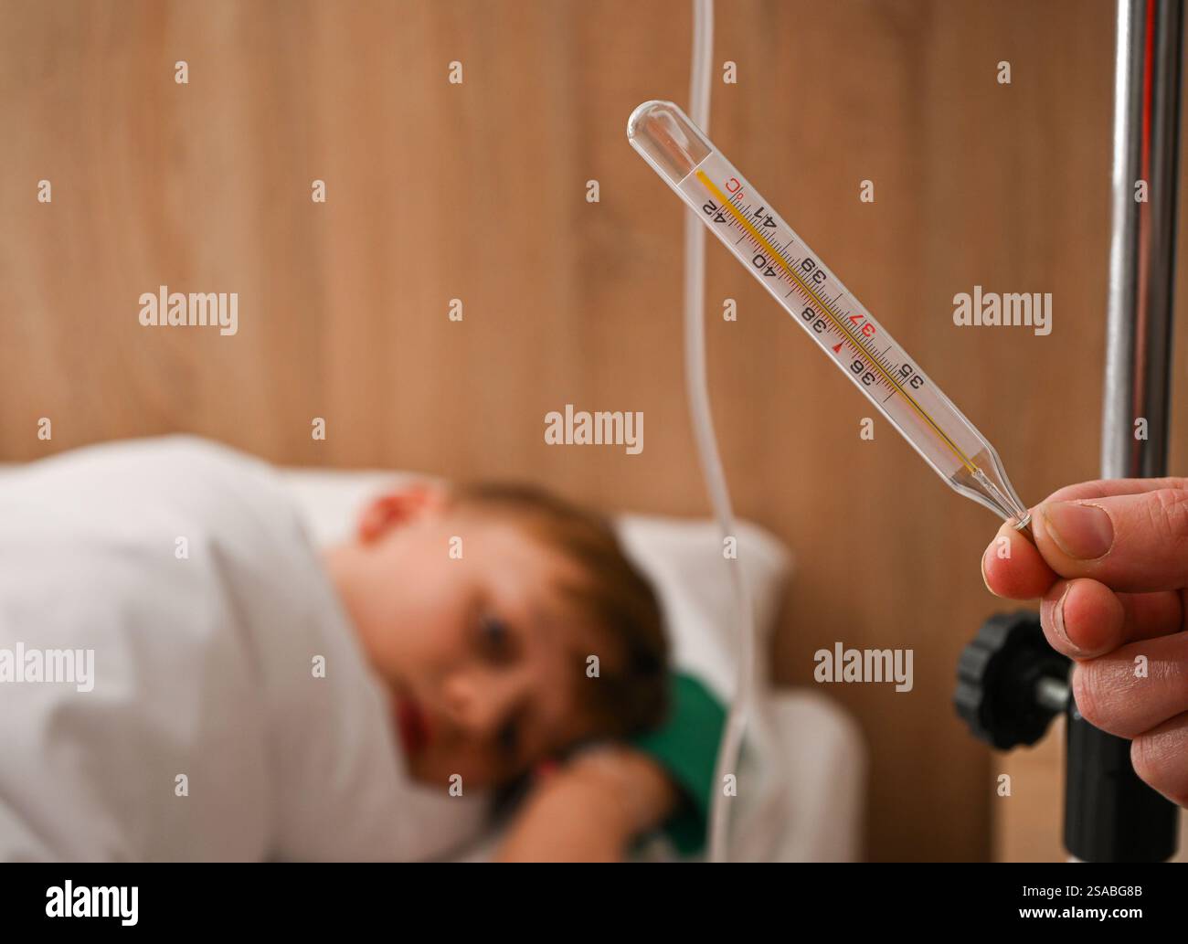 Medico in possesso di termometro a mercurio che mostra febbre, con bambino malato che riposa nel letto d'ospedale sullo sfondo. Foto Stock