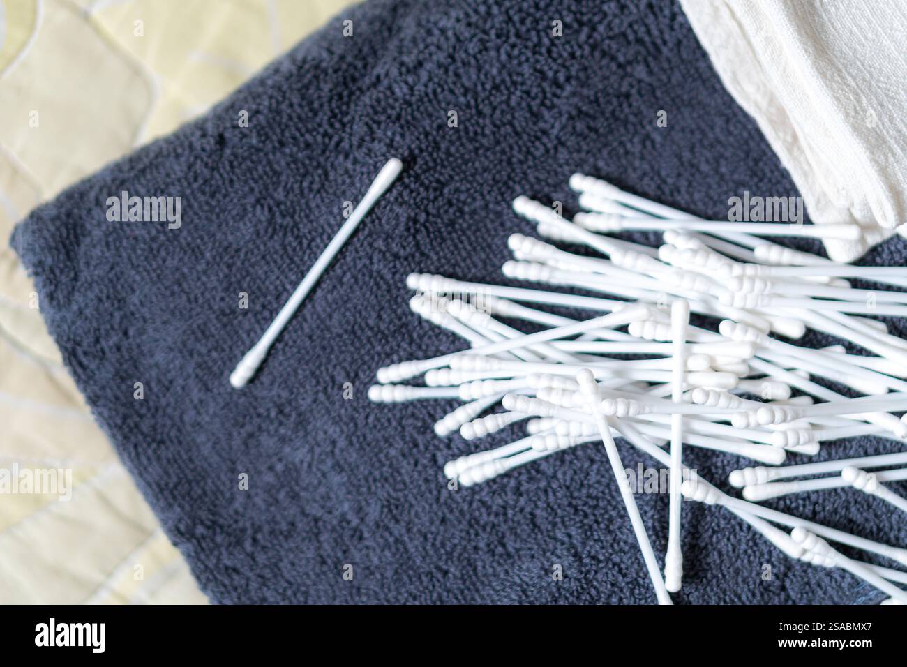 Vista ravvicinata di una pila di bastoncini di cotone bianchi sparsi su un asciugamano scuro, con un panno morbido sullo sfondo. Foto Stock