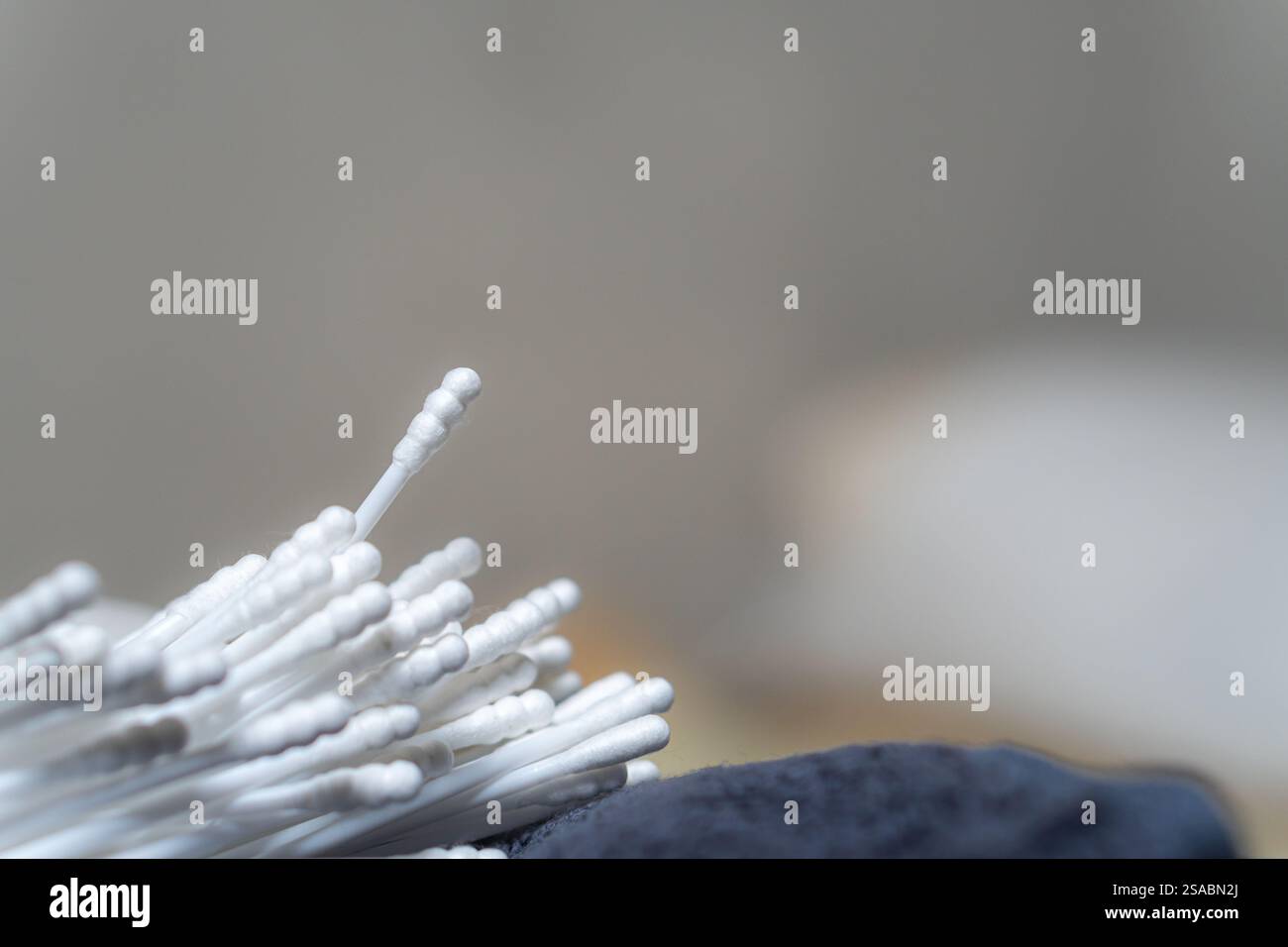 Vista ravvicinata di un mucchio di bastoncini di cotone su una superficie ruvida, con sfondo sfocato. I bastoncini di cotone sono bianchi e disposti in modo casuale, in particolare Foto Stock