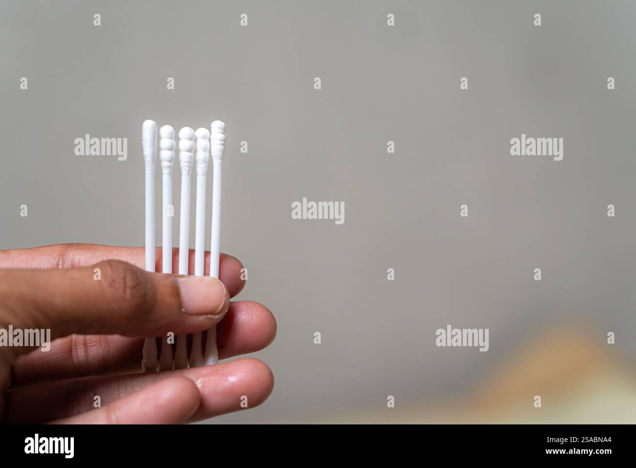 Una mano che tiene diversi bastoncini di cotone su uno sfondo sfocato. I tamponi sono bianchi e ordinatamente disposti nelle dita, mostrando i loro puliti e S Foto Stock