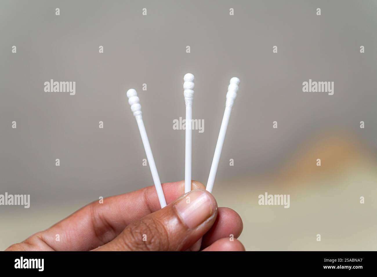 Una mano che tiene tre bastoncini di cotone su uno sfondo sfocato. I tamponi sono bianchi con estremità arrotondate, a dimostrazione del loro design tipico per la pulizia dell'unità pu Foto Stock