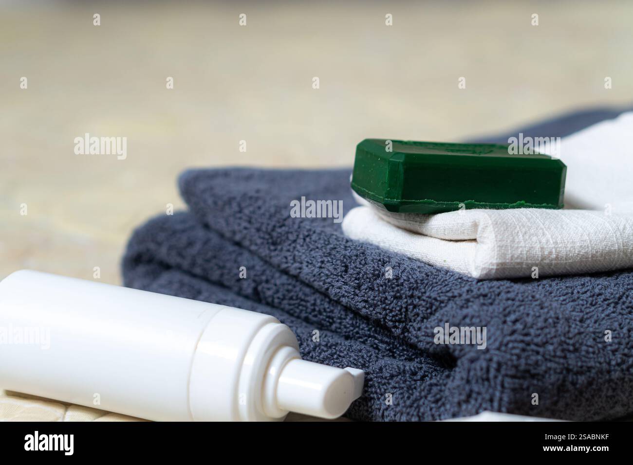 Un primo piano di asciugamani ordinati con una saponetta verde e una bottiglia di lozione bianca. Gli asciugamani sono in colori scuri e chiari, creando un bancomat simile a una spa Foto Stock