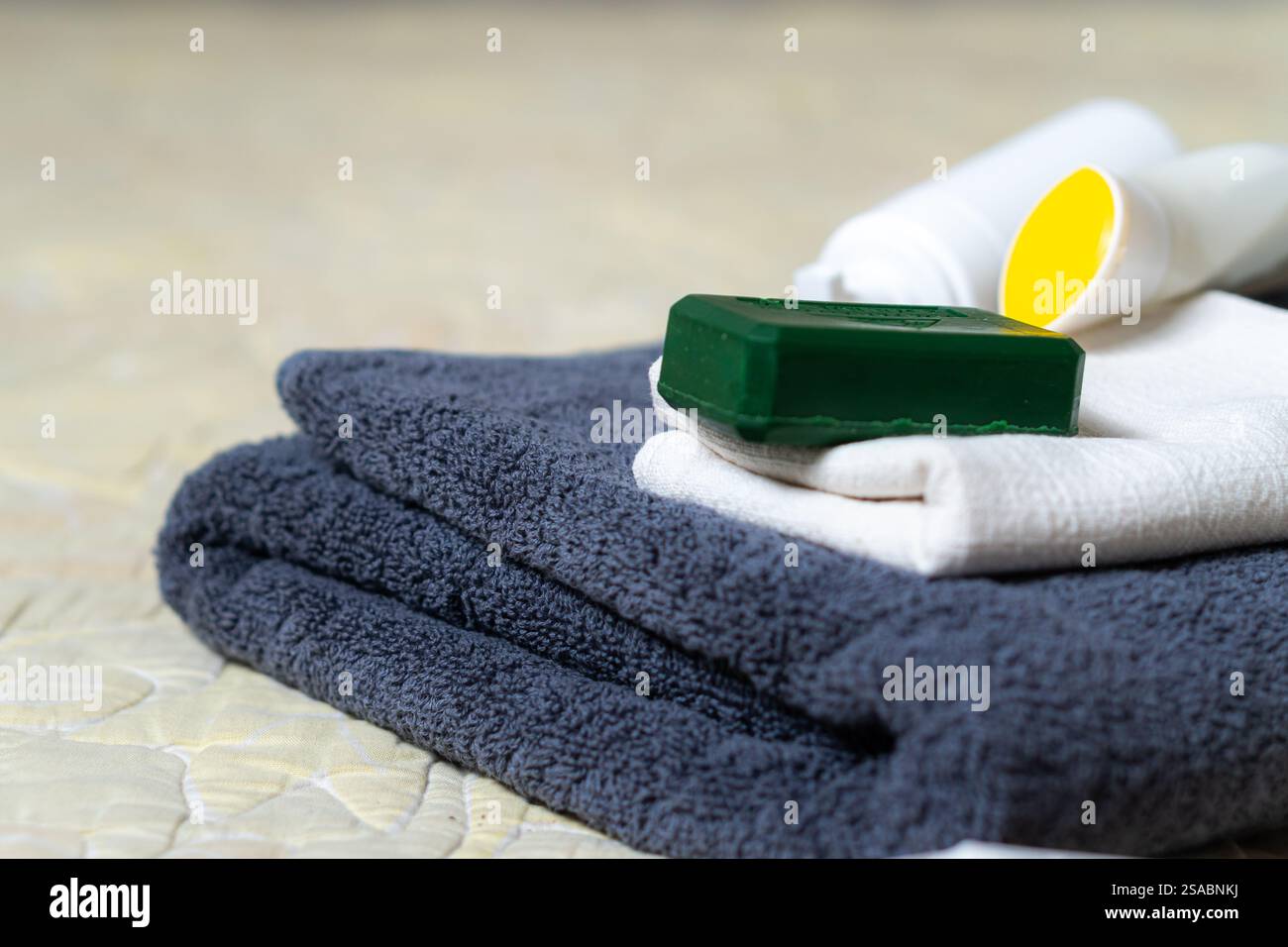 Una pila ordinata di asciugamani nei colori grigio scuro e bianco, accompagnata da una barretta verde di sapone e due bottiglie di lozione o shampoo Foto Stock