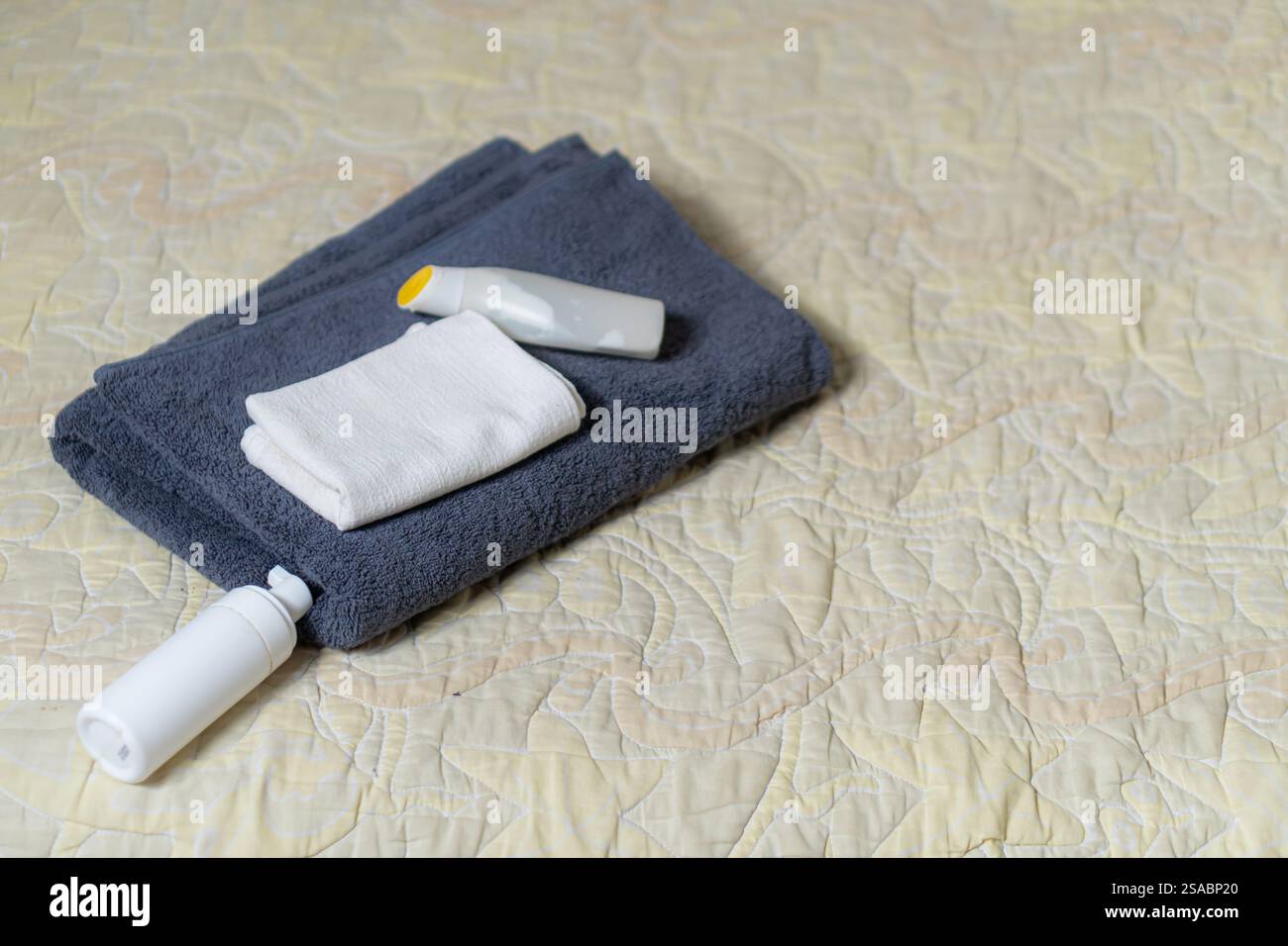 Un set ordinato di asciugamani e articoli da toeletta su un letto. La scena include un asciugamano grigio scuro, un piccolo asciugamano bianco e due bottiglie di lozione o shamp Foto Stock