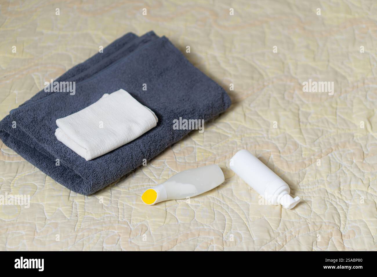 Un set ordinato di asciugamani e prodotti da bagno su un copriletto a motivi geometrici. L'immagine presenta una pila di asciugamani blu scuro, un piccolo asciugamano bianco e due Foto Stock