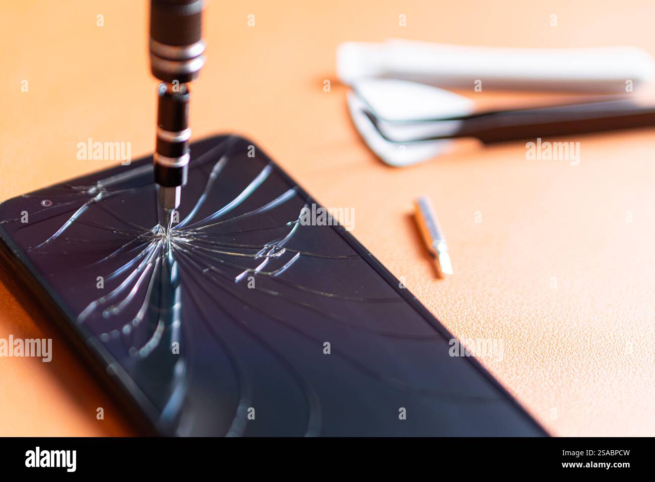 Primo piano di un set di cacciaviti di precisione con punte multiple, un portautensili giallo e uno smartphone con schermo incrinato su una superficie arancione. Foto Stock