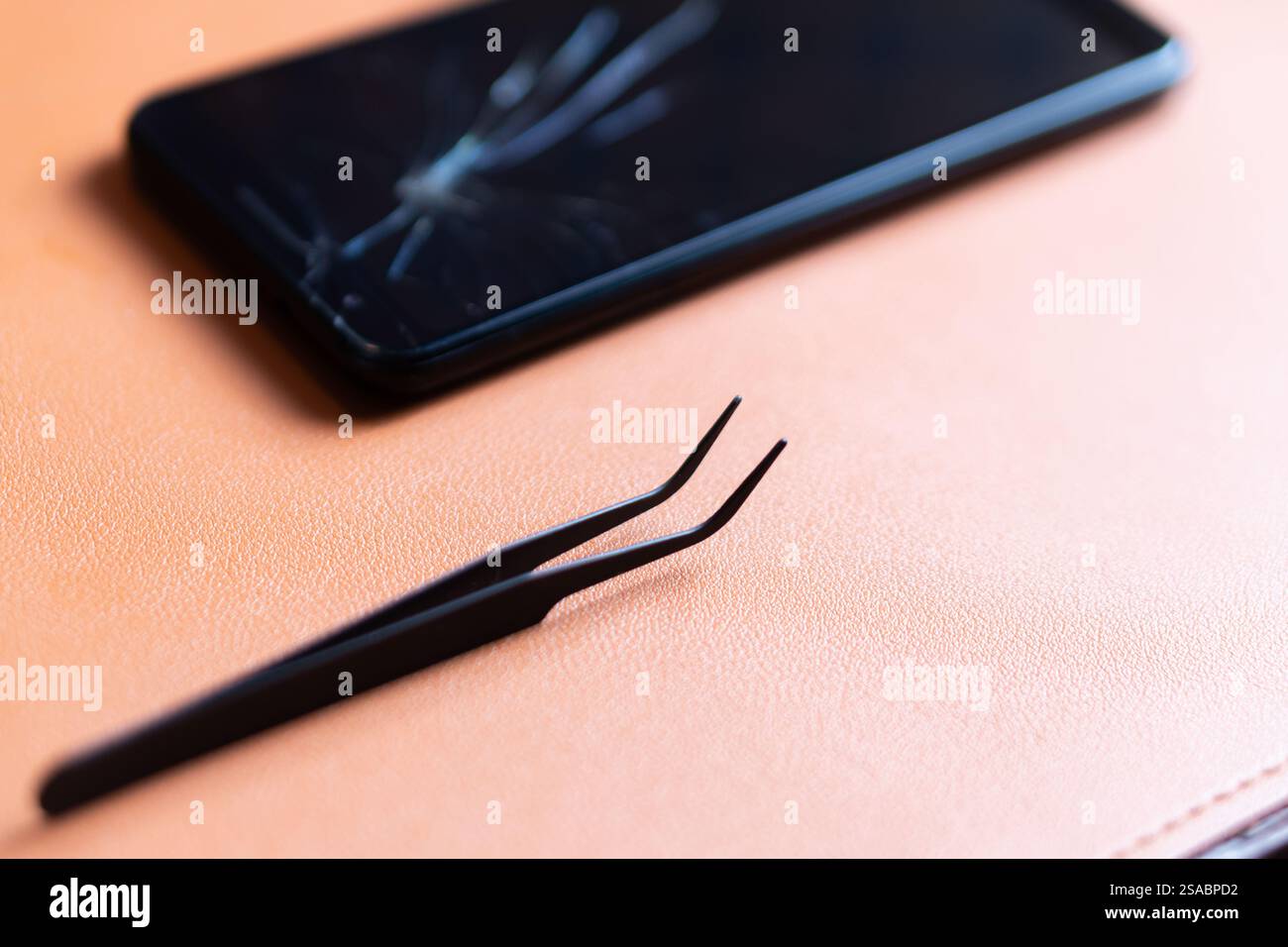 Vista ravvicinata dello schermo di uno smartphone rotto con un display incrinato, posizionato su una superficie in pelle testurizzata. Accanto al telefono, ci sono le pinzette nere Foto Stock