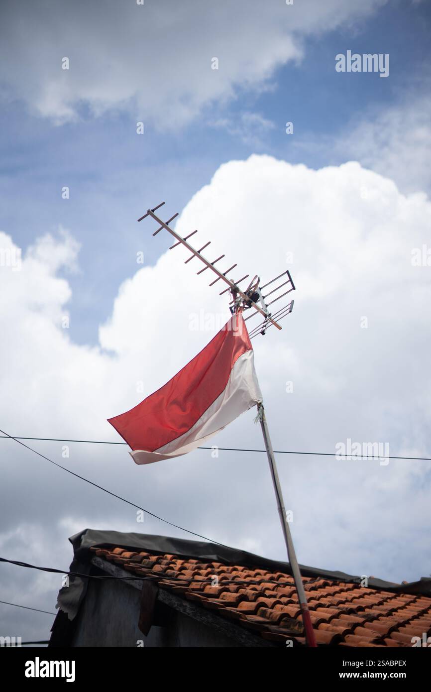 Bandiera indonesiana che sventola orgogliosamente sotto un'antenna televisiva contro un cielo nuvoloso. Foto Stock