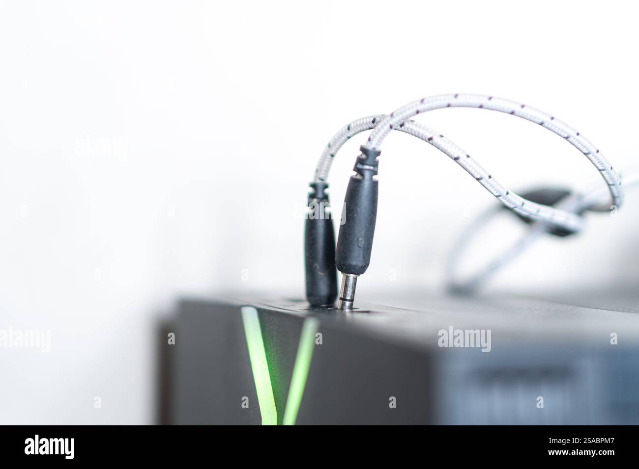 Primo piano di un jack audio nero collegato a un dispositivo, con sfondo sfocato. Il dispositivo è dotato di luci LED verdi che suggeriscono un gioco o una tecnologia Foto Stock
