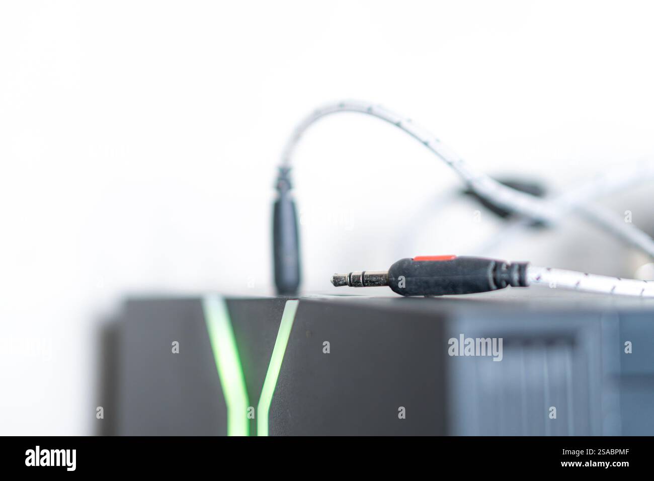 Primo piano di un jack audio nero collegato a un dispositivo, con sfondo sfocato. Il dispositivo è dotato di luci LED verdi che suggeriscono un gioco o una tecnologia Foto Stock