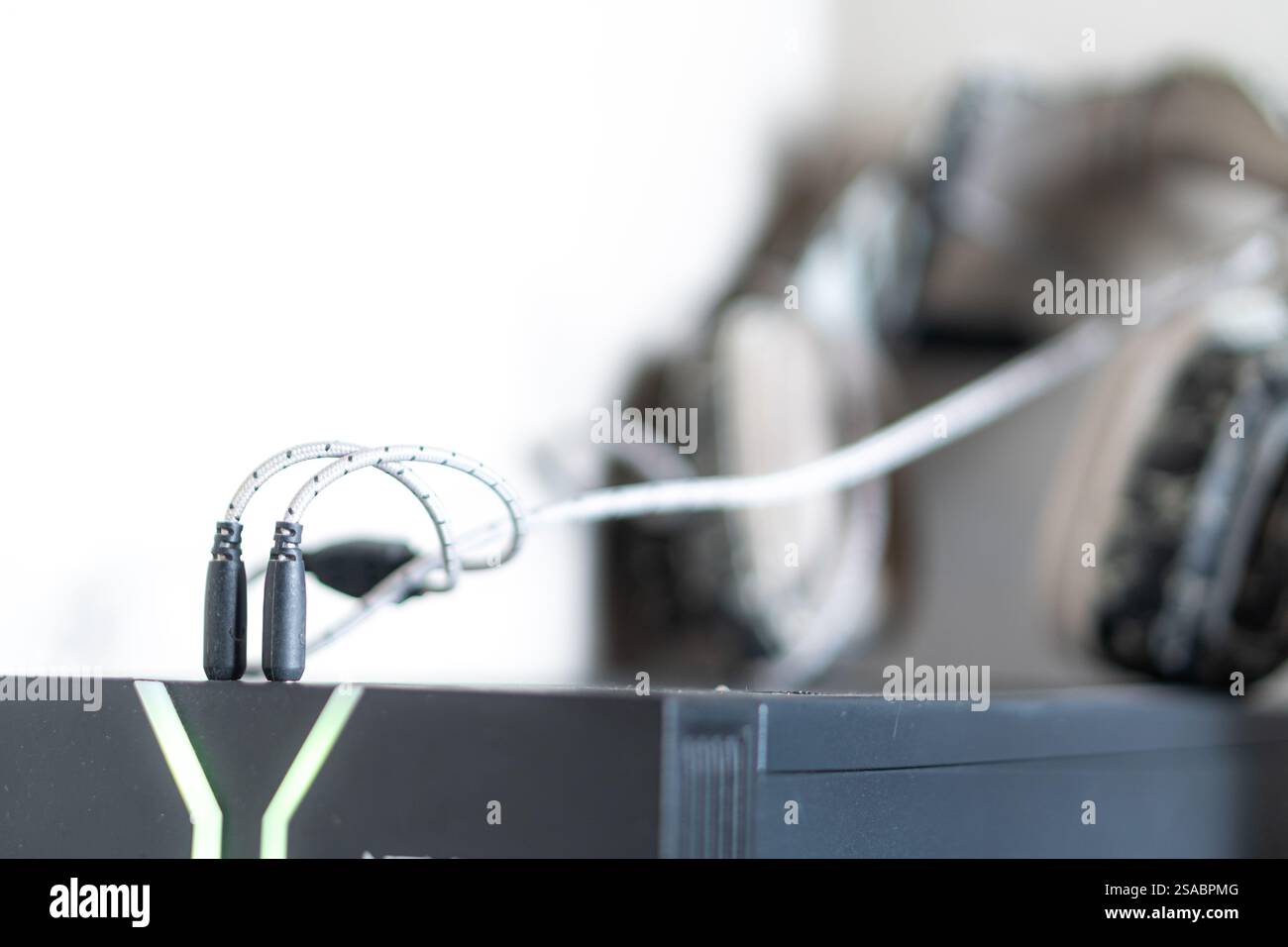 Primo piano di un jack audio nero collegato a un dispositivo, con sfondo sfocato. Il dispositivo è dotato di luci LED verdi che suggeriscono un gioco o una tecnologia Foto Stock