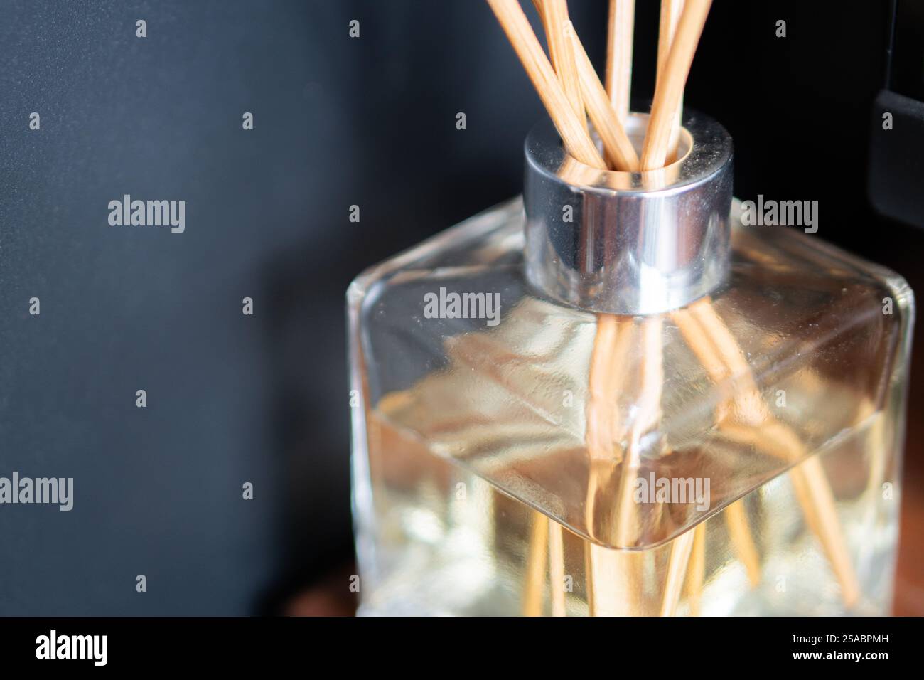 Un elegante diffusore in vetro con canne in legno siede su una scrivania, accanto a una candela illuminata. Lo sfondo presenta una tastiera per computer e uno schermo leggermente illuminato, Foto Stock