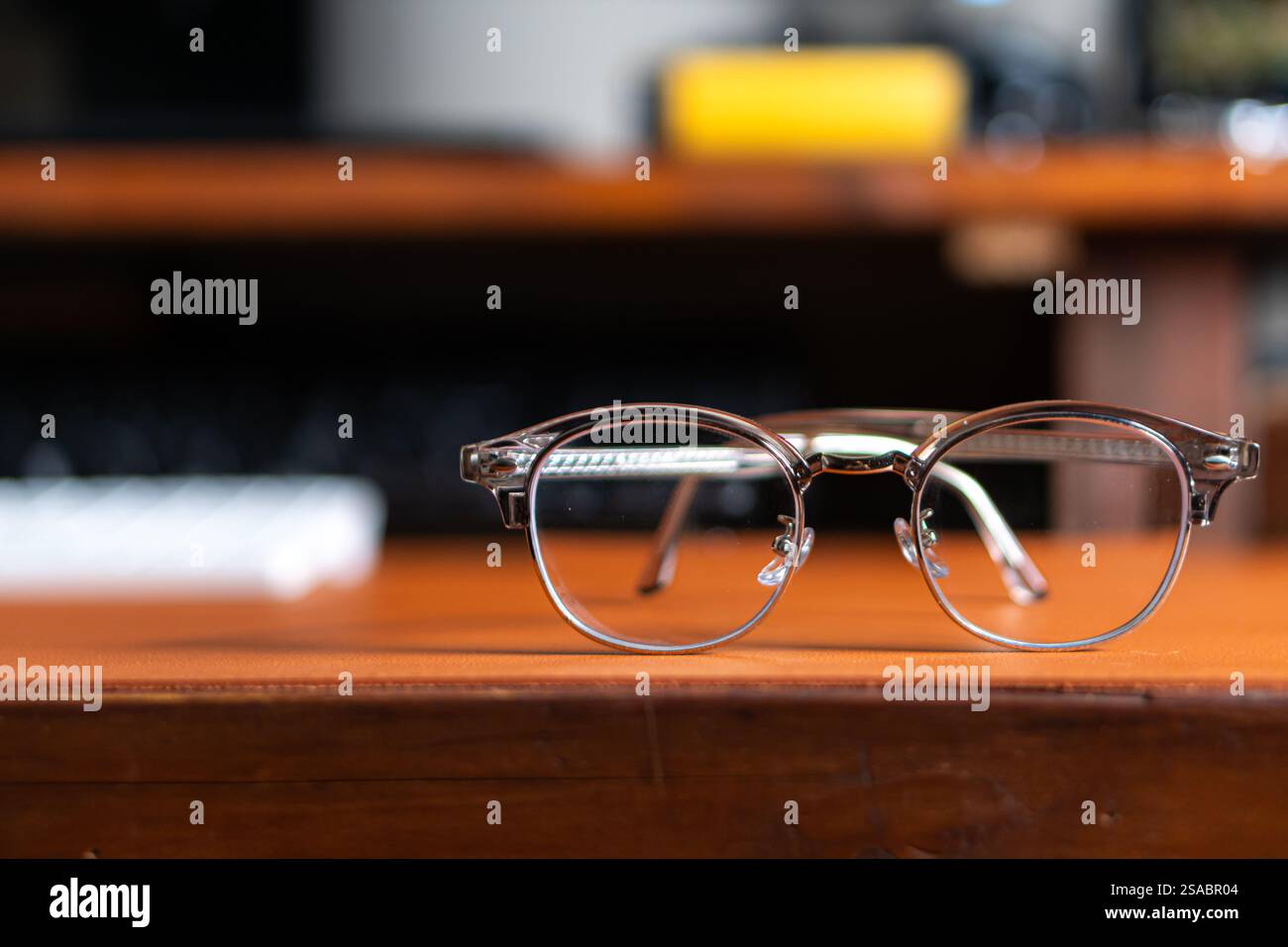 Un paio di eleganti occhiali da vista appoggiati su una superficie in pelle marrone, con una tastiera sfocata sullo sfondo. Foto Stock