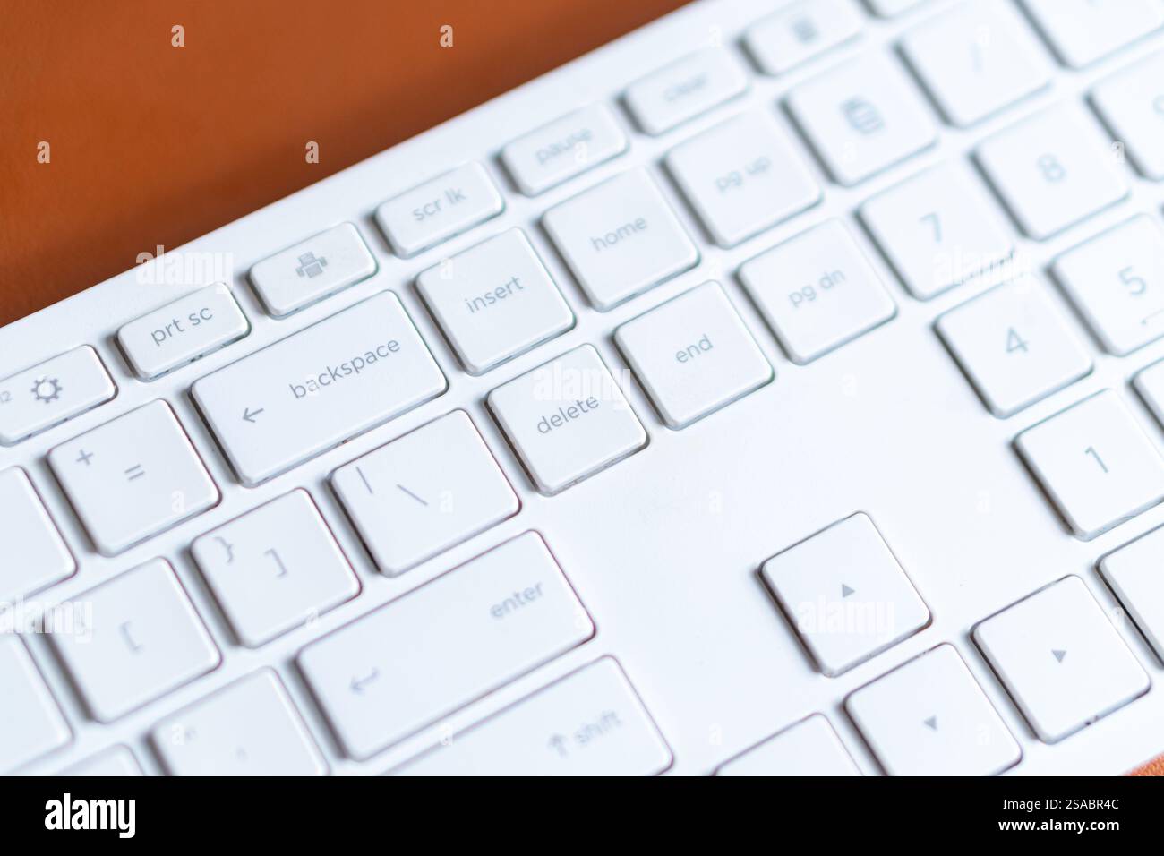 Vista ravvicinata di una tastiera bianca per computer con tastierino numerico su una superficie marrone. Foto Stock
