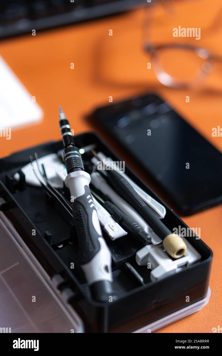 Vista ravvicinata di un kit di utensili contenente vari cacciaviti e utensili, posizionato su una scrivania accanto a uno smartphone e a una tastiera. Foto Stock