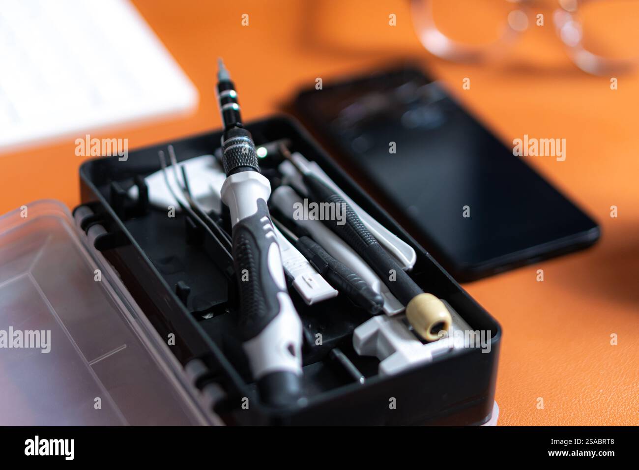 Vista ravvicinata di un kit di utensili contenente vari cacciaviti e utensili, posizionato su una scrivania accanto a uno smartphone e a una tastiera. Foto Stock