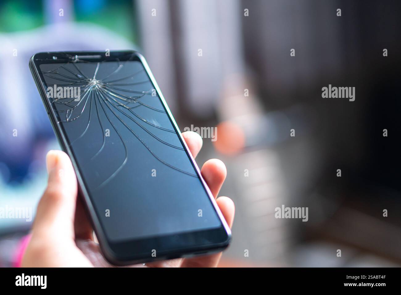 Primo piano di una mano che tiene in mano uno smartphone con uno schermo incrinato su uno sfondo bianco. Lo schermo è scuro e mette in evidenza il tipo ragnatela Foto Stock