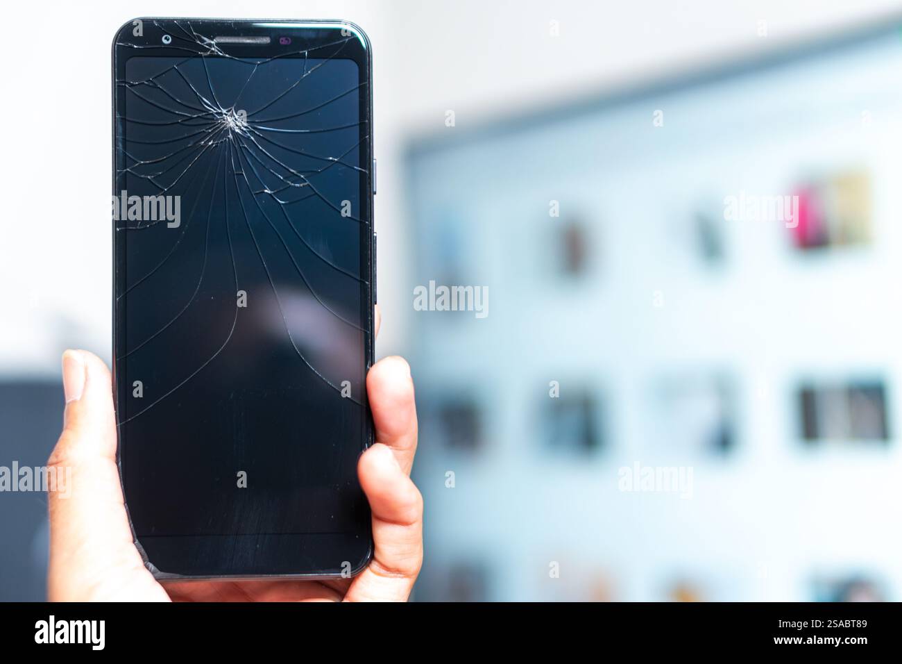 Primo piano di una mano che tiene in mano uno smartphone con uno schermo incrinato su uno sfondo bianco. Lo schermo è scuro e mette in evidenza il tipo ragnatela Foto Stock