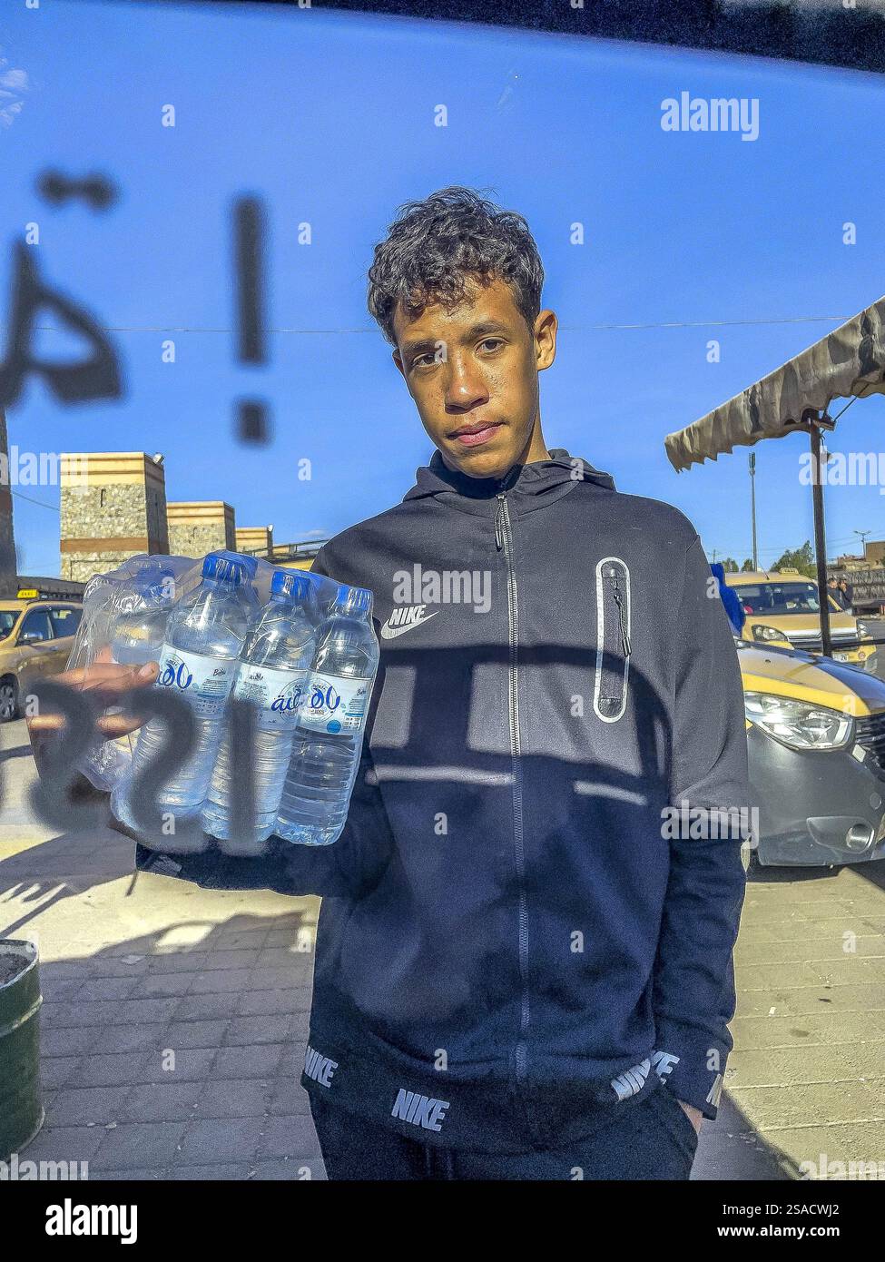 Giovane che vende acqua in una stazione di taxi a lunga distanza a Marrakech, Marocco Foto Stock