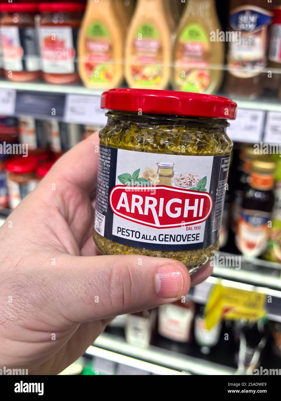 Bobruisk, Bielorussia - 26 gennaio 2025: Una mano si avvicina a un vaso di pesto in un colorato corridoio di alimentari, circondato da varie salse e condimenti. Foto Stock