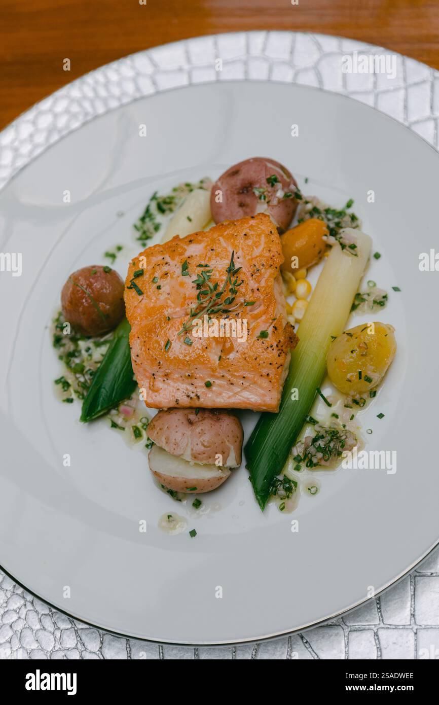 Un filetto di salmone perfettamente grigliato si trova su un letto di colorate verdure di stagione, guarnite con erbe fresche. Il piatto è presentato su un piatto elegante Foto Stock