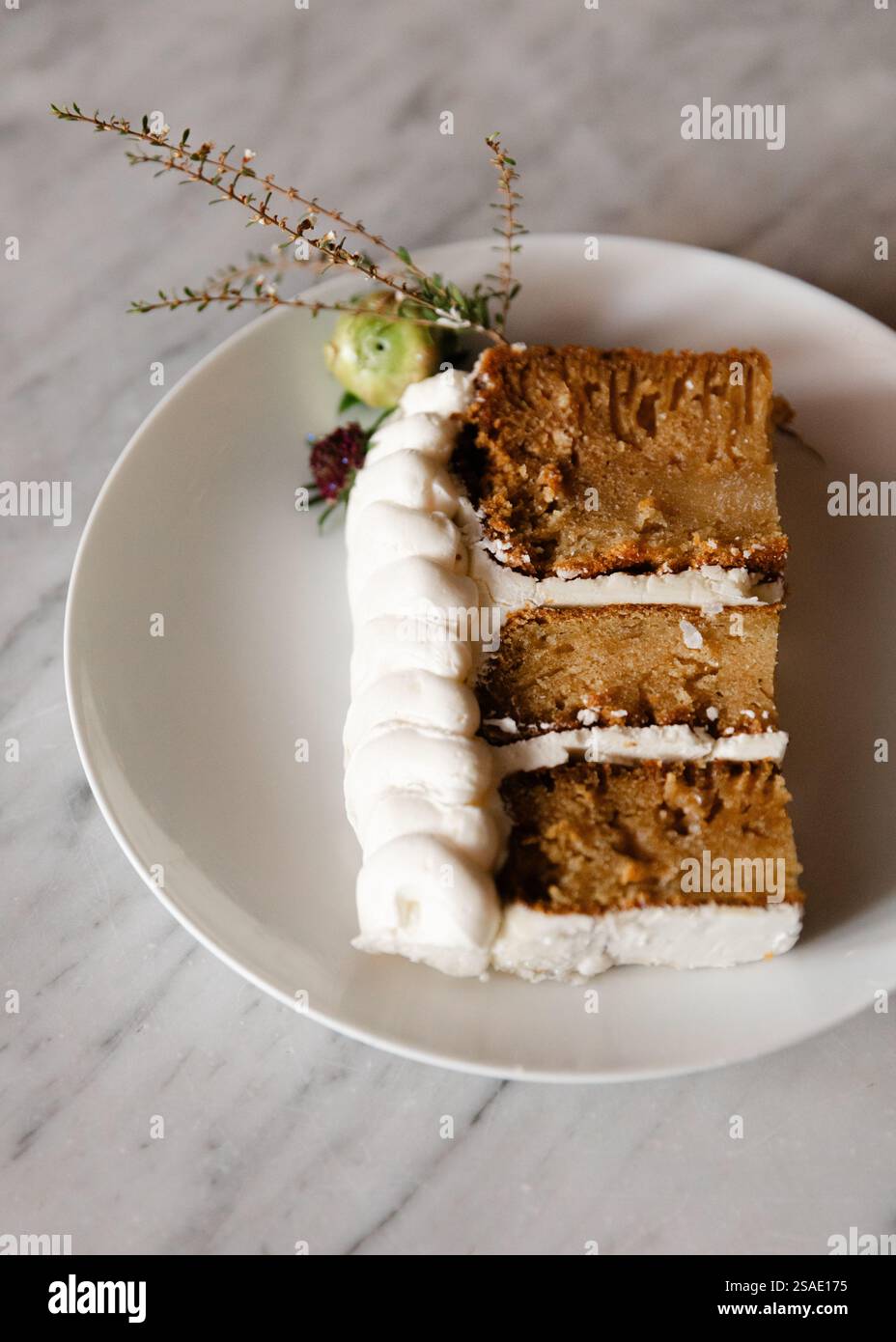 Una fetta di torta ben presentata presenta una glassa cremosa ed è decorata con delicati fiori e vegetazione. La torta si appoggia su una W pulita Foto Stock