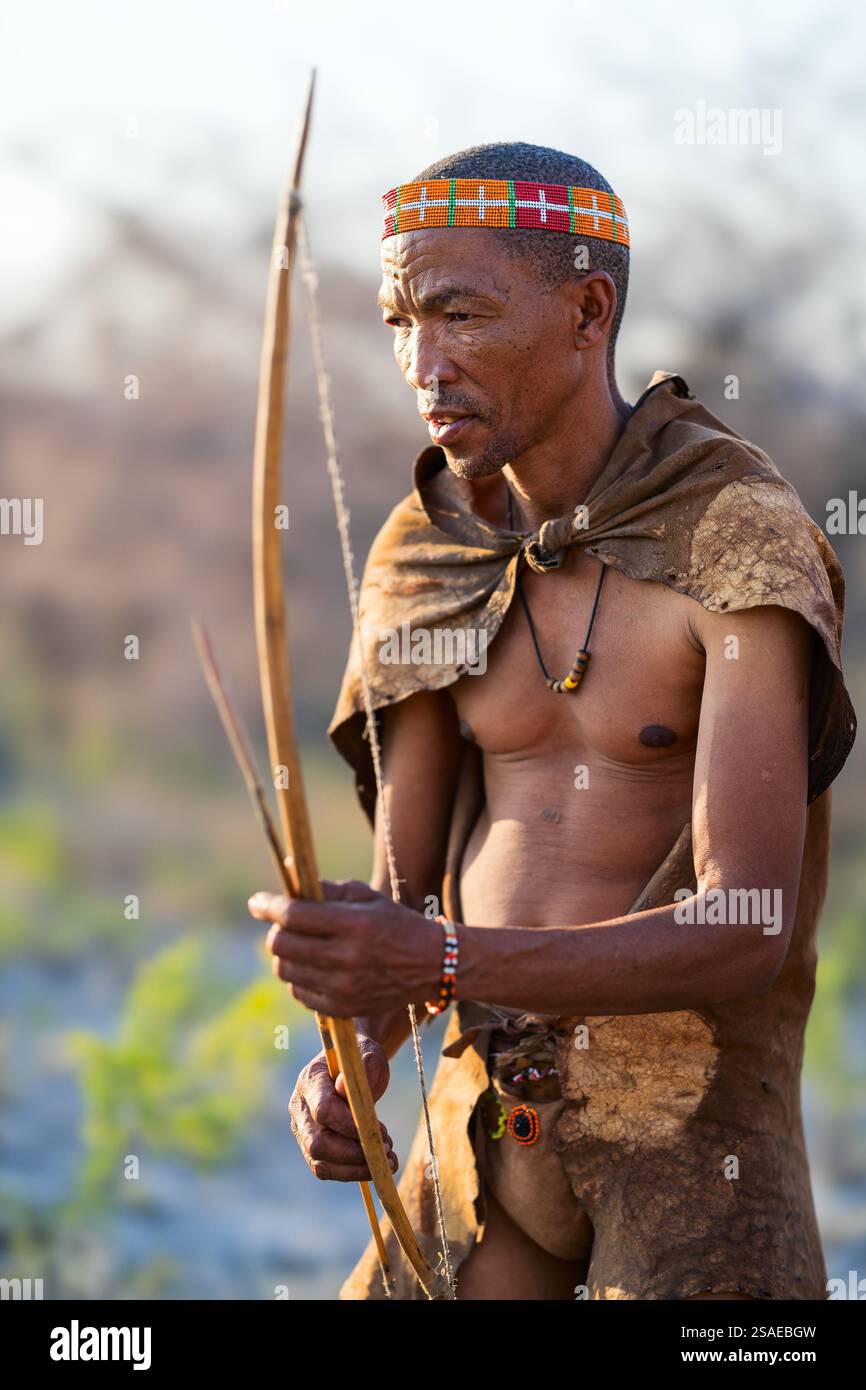 Makgadikgadi Pans, Botswana - 14 luglio 2024: Cacciatore di Boscimani che indossa un abbigliamento tradizionale, tenendo un arco e una freccia artigianali, mostrando la sua abilità e la sua abilità Foto Stock