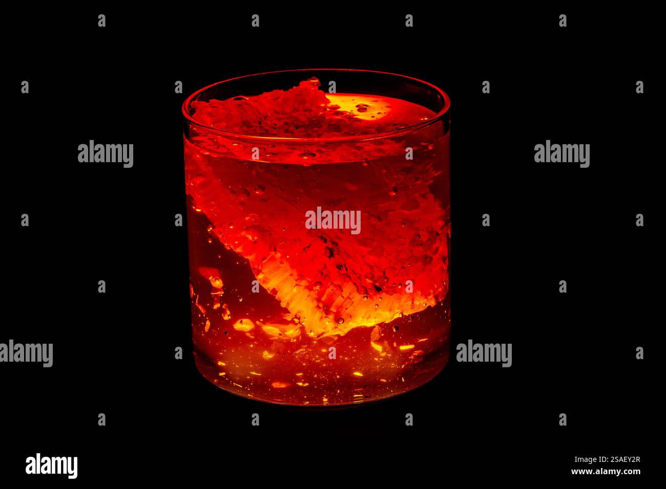 Nido d'ape immerso in un vaso di miele, con colori caldi e vivaci come l'arancione, il giallo e il rosso, il tutto su uno sfondo nero pieno. Foto Stock