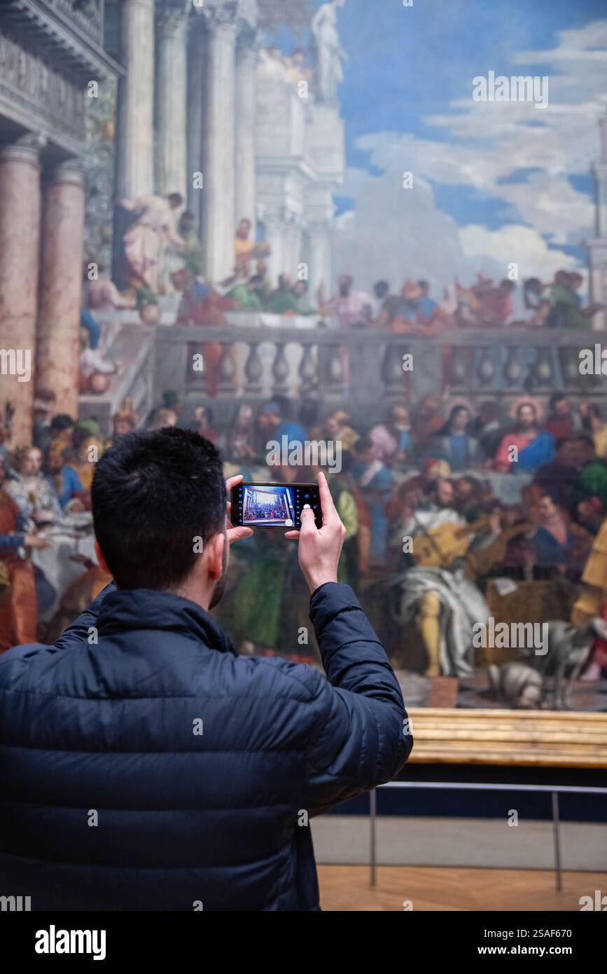 Un visitatore fotografa il dipinto „Les Noces de Cana“ (il matrimonio a Cana) di Paolo Veronese al Museo del Louvre di Parigi, Francia. Foto Stock