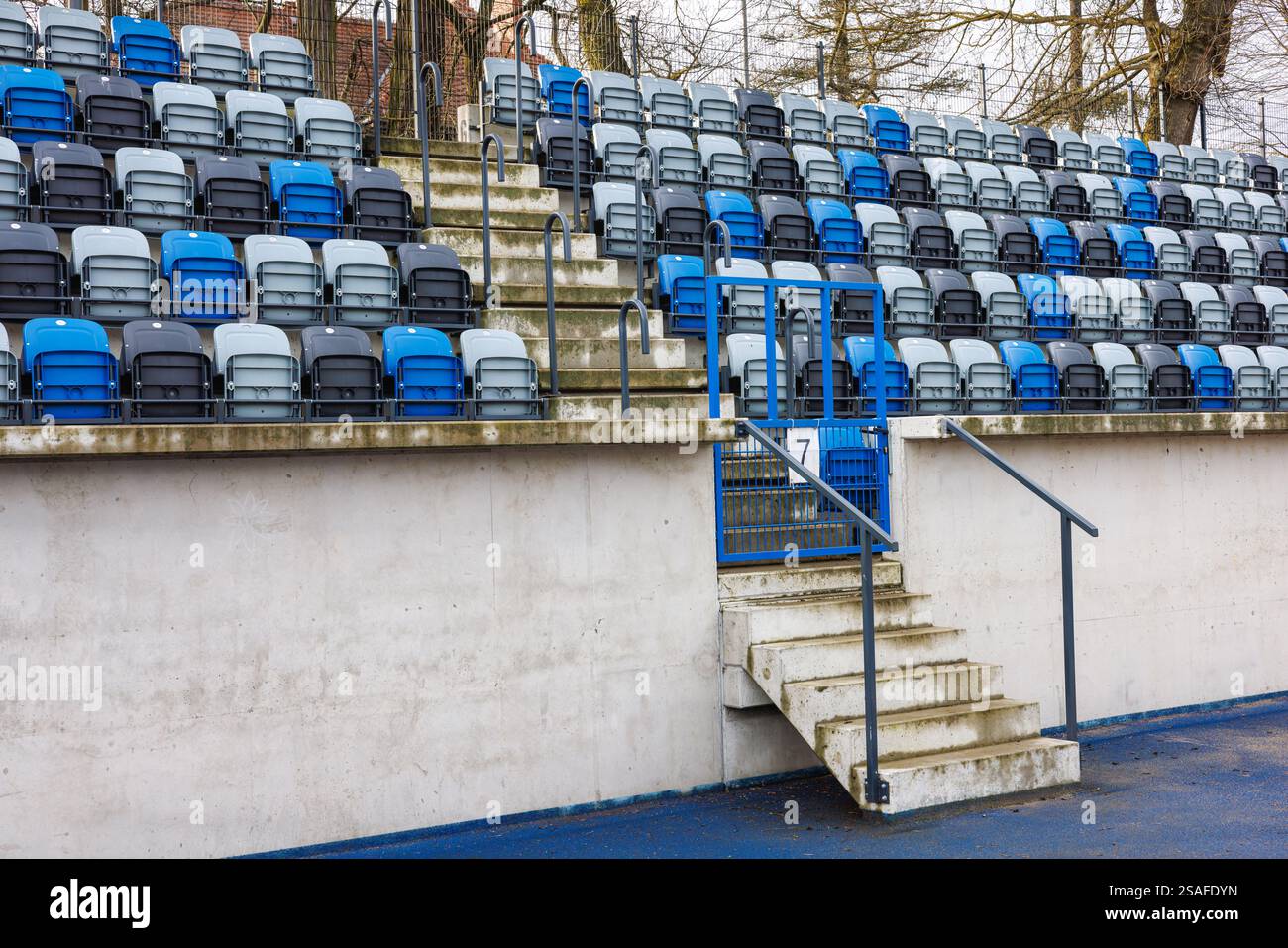File di posti numerati blu e grigio in uno stadio vicino a una corsia con gradini di cemento. Foto Stock