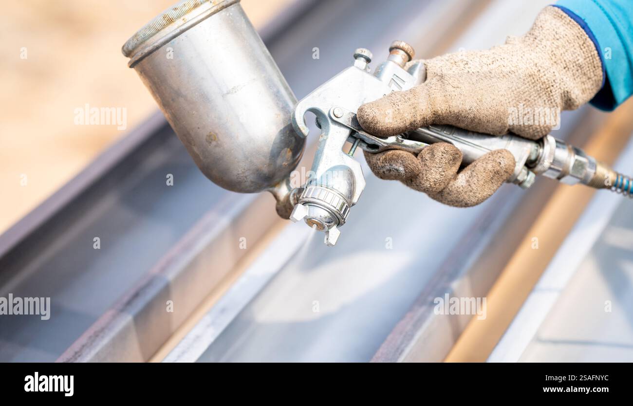 Il lavoratore edile dipinge il rivestimento superficiale della struttura metallica con una pistola a spruzzo in cantiere. Protezione contro la corrosione e la ruggine dei metalli. Industriale Foto Stock