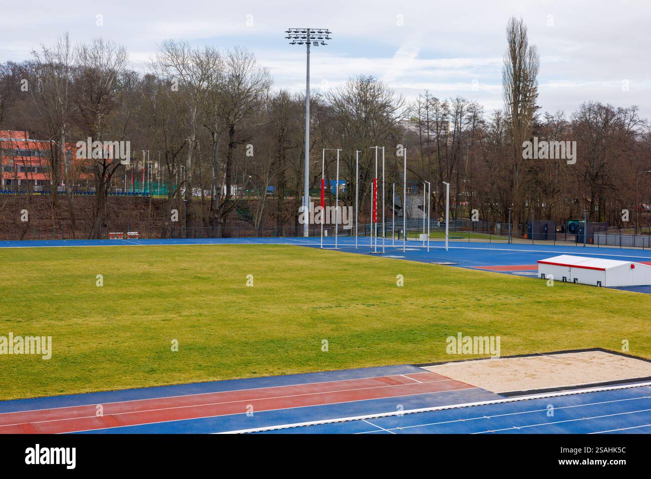 Campo da calcio con erba artificiale e piste da corsa blu. Stadio cittadino con un parco intorno. Pozzo di sabbia per saltare. Foto Stock