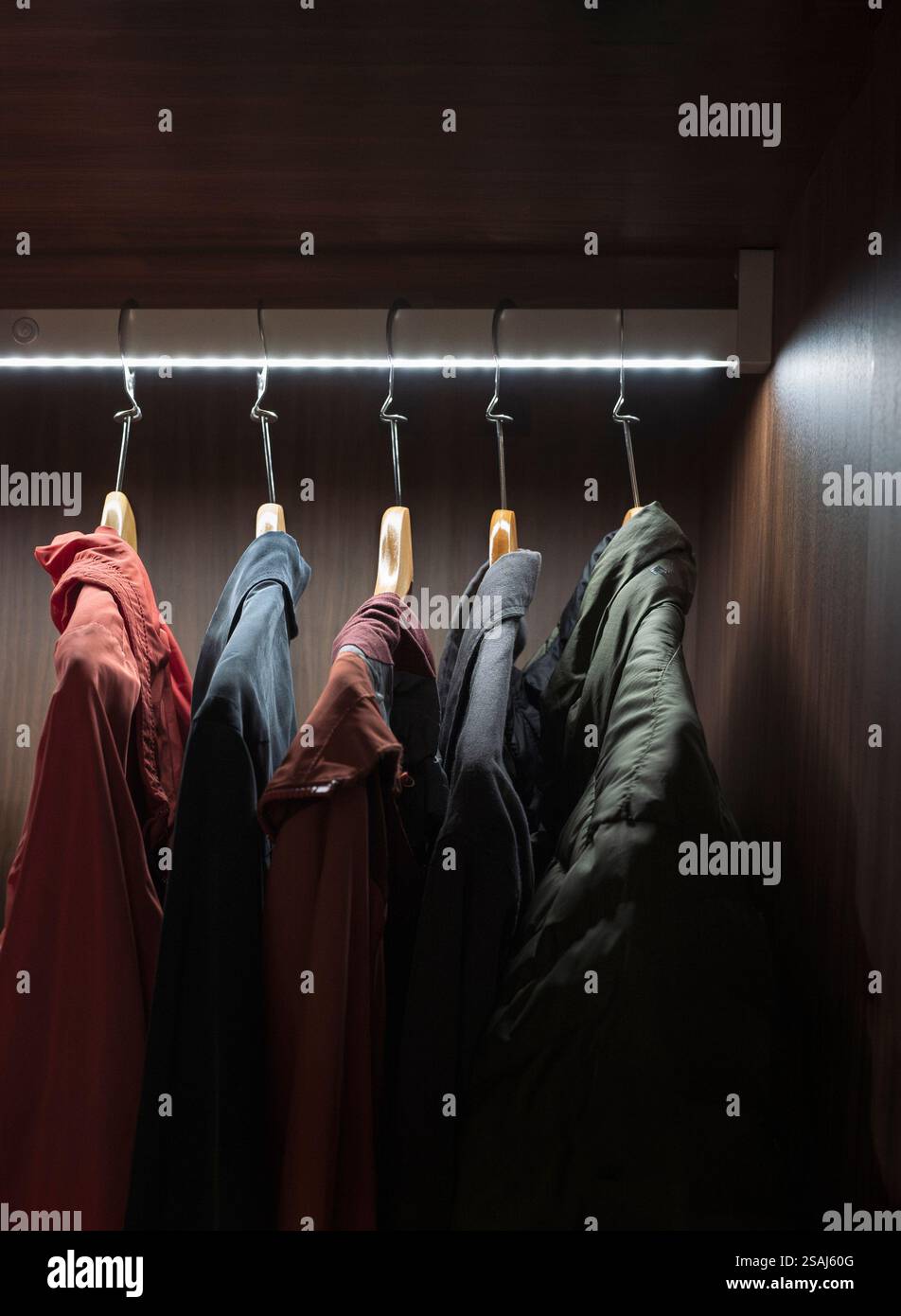Disordine nell'armadio. Abiti informali appesi nell'armadio con illuminazione a LED Foto Stock