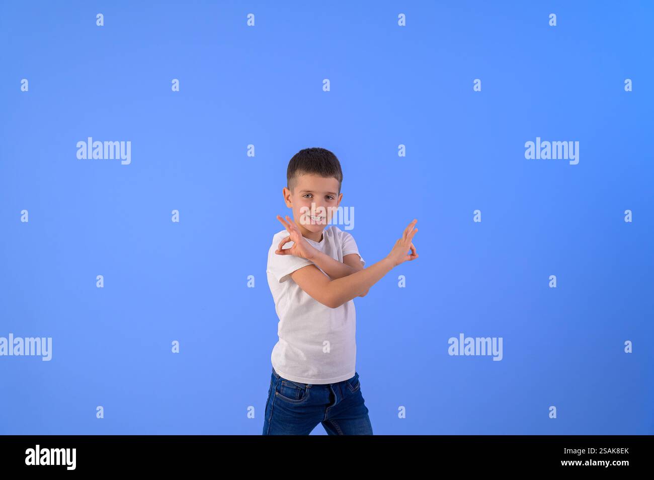 Ritratto di un ragazzo carino che attraversa le mani e mostra segni di OK mentre si trova su uno sfondo blu isolato Foto Stock