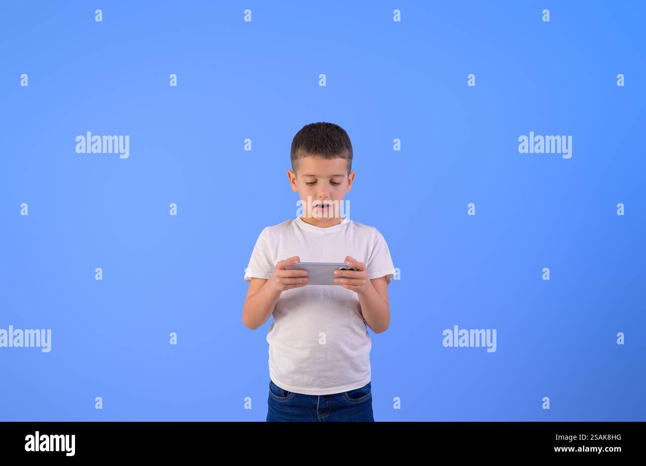 Ritratto di un piccolo uomo d'affari che gioca ai videogame su uno smartphone mentre si trova su uno sfondo blu Foto Stock