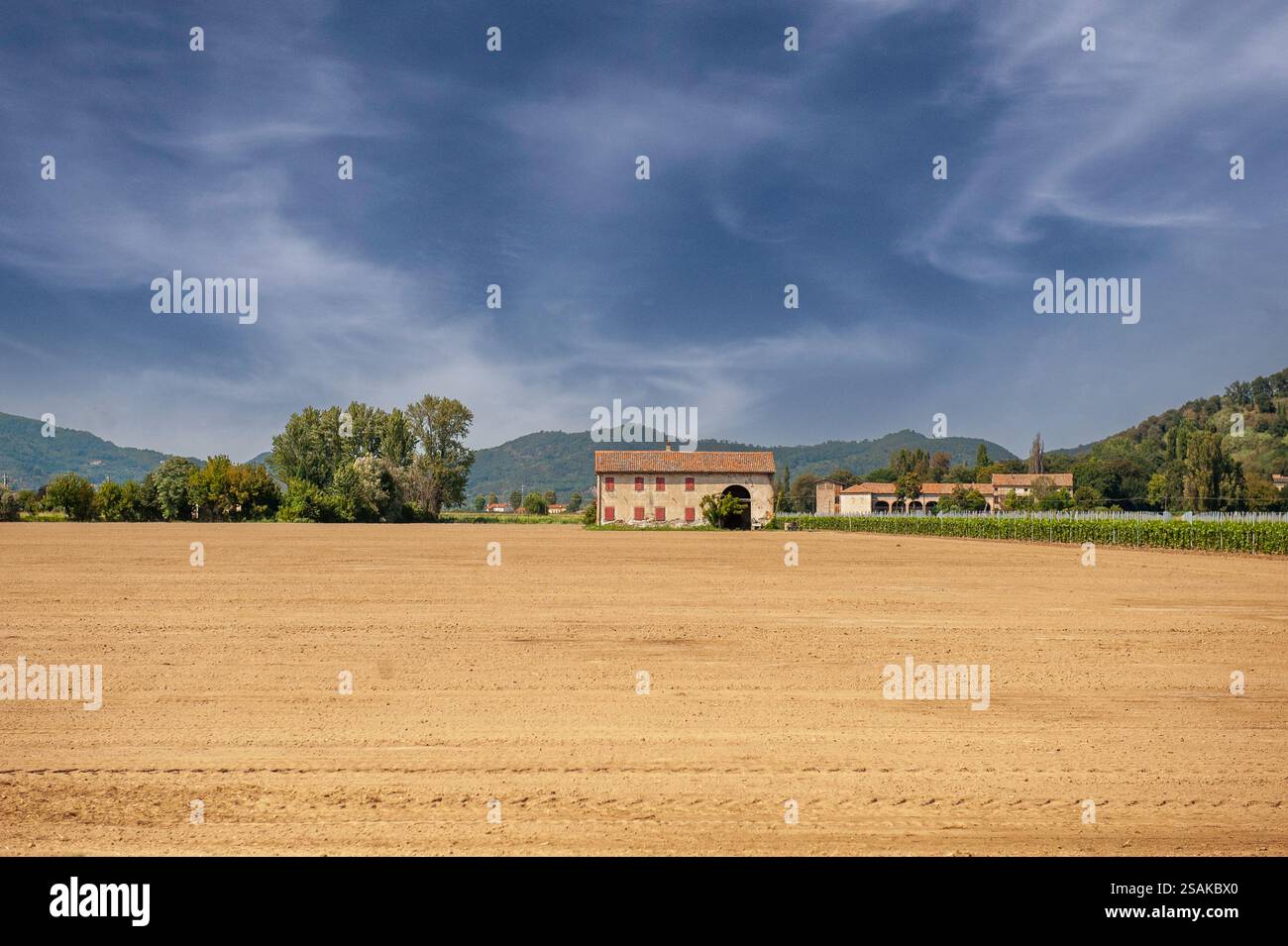 Vista panoramica di una fattoria tradizionale circondata da campi agricoli in Emilia-Romagna, Italia, con colline e paesaggi di campagna sotto un drammaturgo Foto Stock