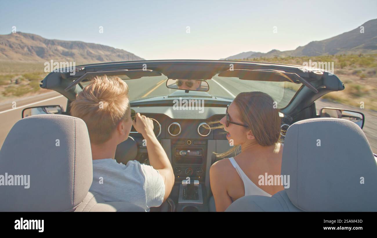 Vista posteriore della coppia giovane durante il viaggio in auto con capote lungo la strada di campagna Foto Stock