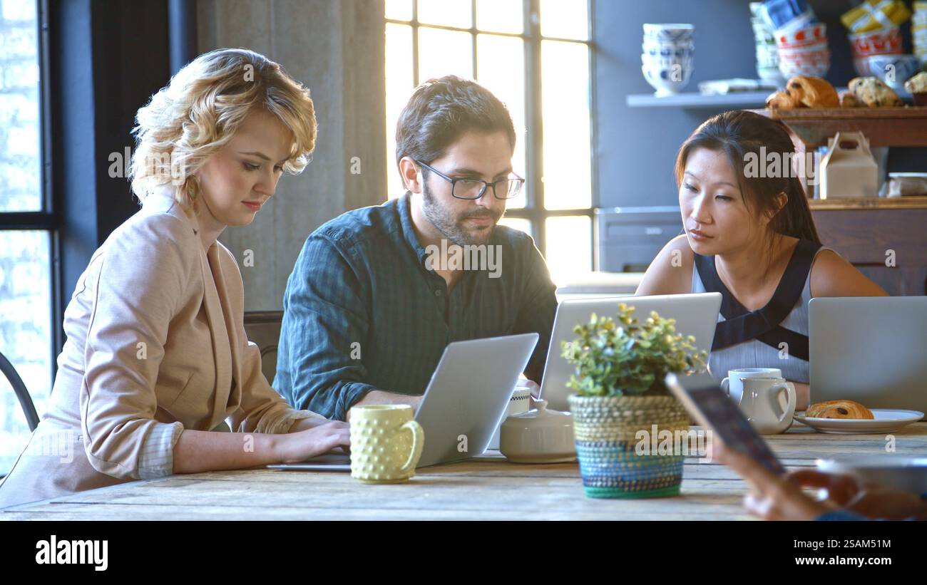 Tre uomini d'affari seduti al tavolo che lavorano al computer portatile nel bar Foto Stock