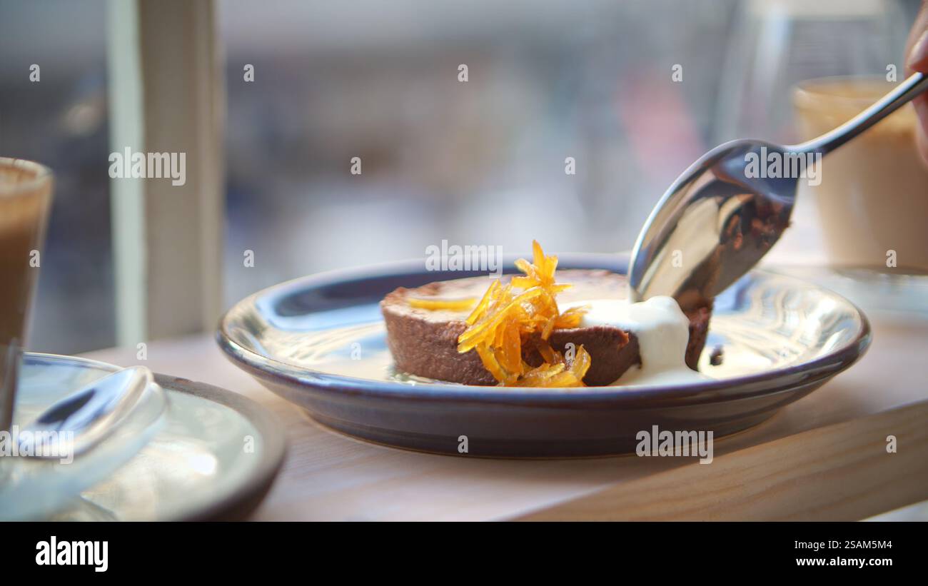 Primo piano di una persona che mangia Chocolate Brownie seduto al finestrino del Cafe' Foto Stock