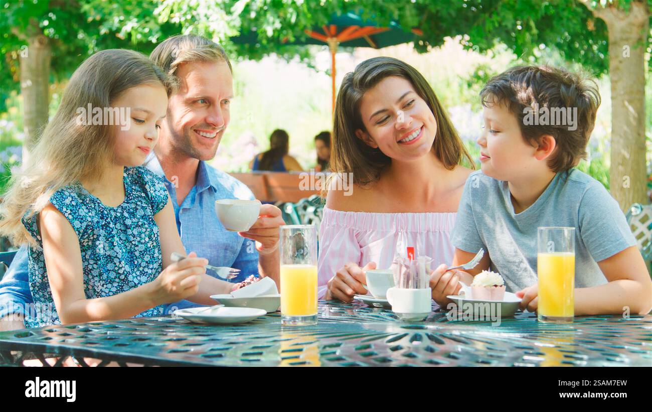La famiglia sedeva al tavolo gustando uno spuntino al Cafe o al ristorante all'aperto Foto Stock