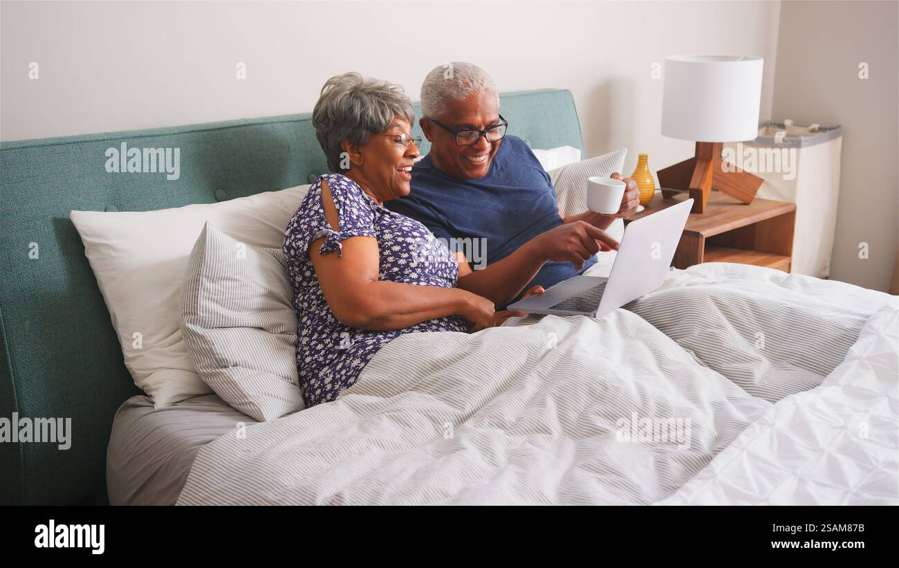 Coppia senior a casa sdraiata a letto con videochiamata con i parenti sul laptop Foto Stock