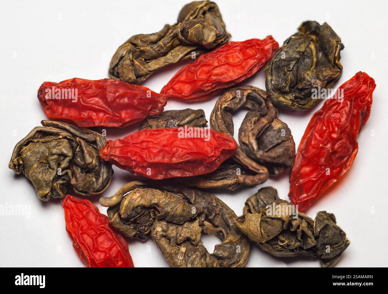 Primo piano di bacche di goji secche miste e foglie di tè verde arrotolate per la preparazione del tè. Foto Stock