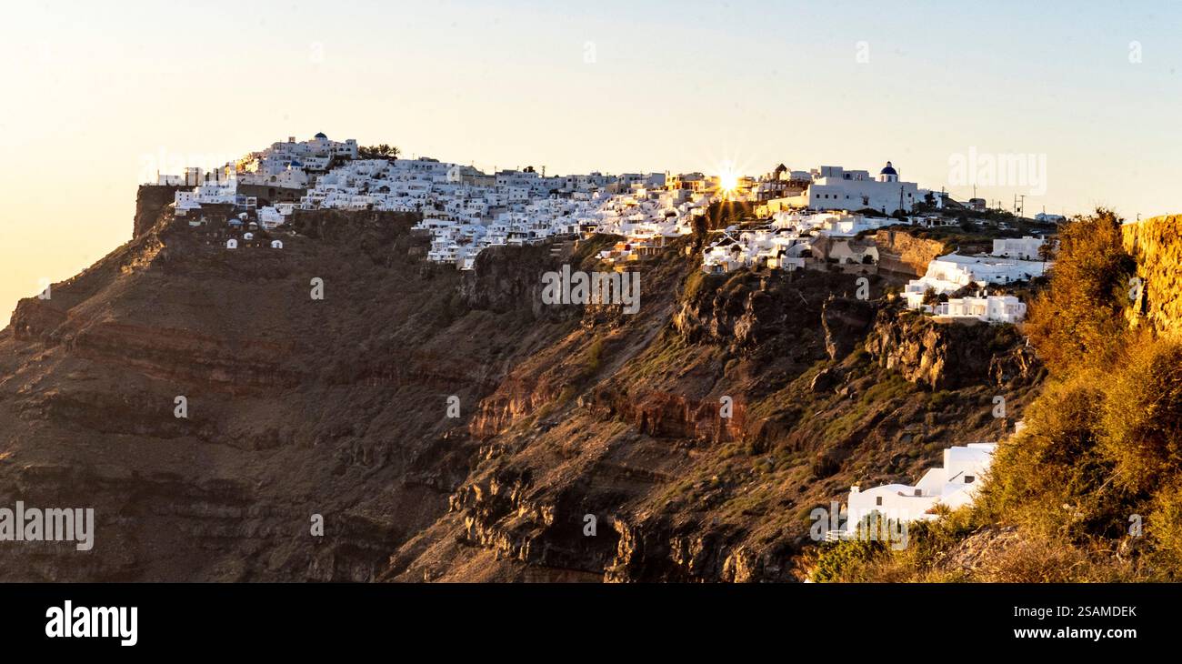 Una vista panoramica di Santorini, Grecia, con edifici dipinti di bianco arroccati su una scogliera durante il tramonto. Il sole proietta una calda luce sulla landsca Foto Stock