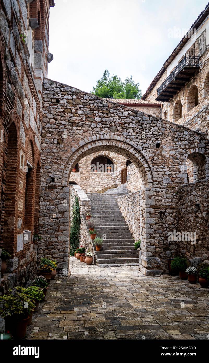 Un pittoresco vicolo in pietra con un arco che conduce ad una scala. Le pareti sono fatte di pietre rustiche e piante in vaso lungo il percorso. La scena io Foto Stock