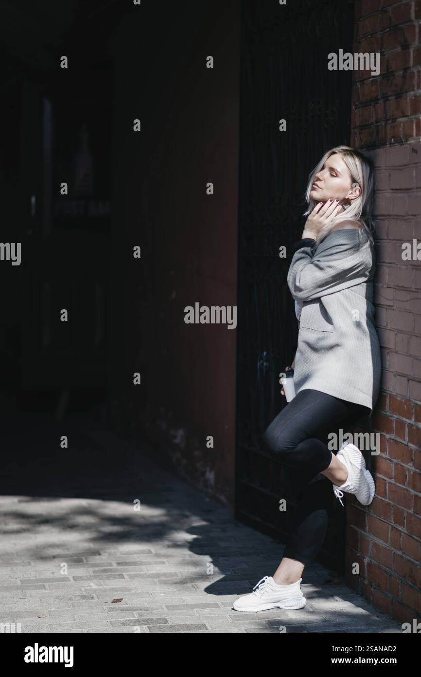 Donna informale appoggiata su un muro di mattoni in un'area ombreggiata Foto Stock
