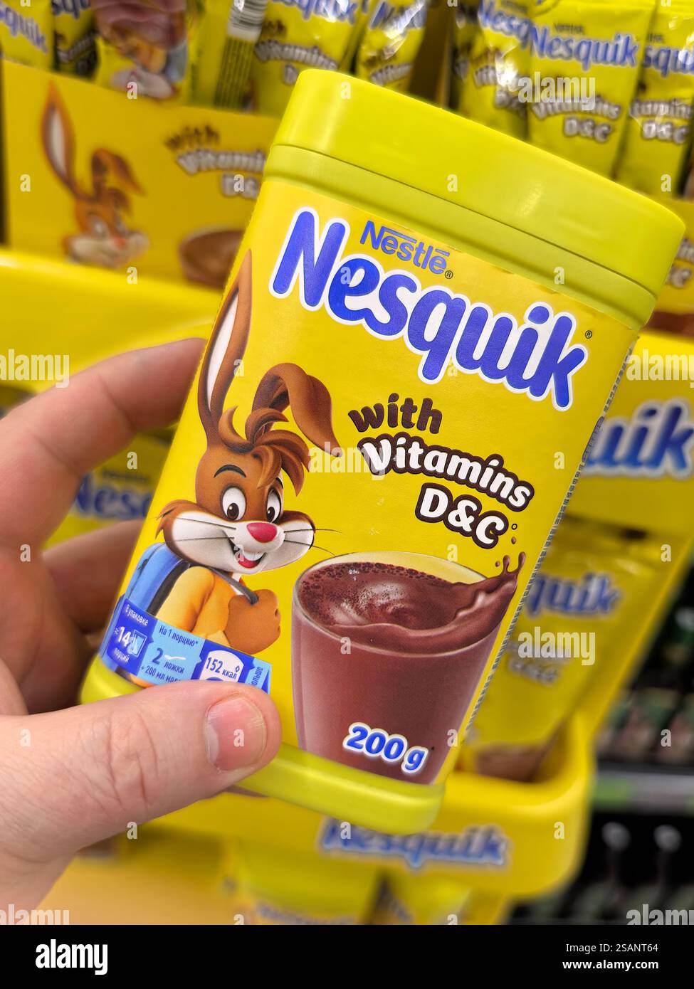 Bobruisk, Bielorussia - 26 gennaio 2025: Una persona sta tenendo in mano un vibrante contenitore di polvere di cioccolato in un corridoio di alimentari. Il contenitore presenta un allegro Foto Stock