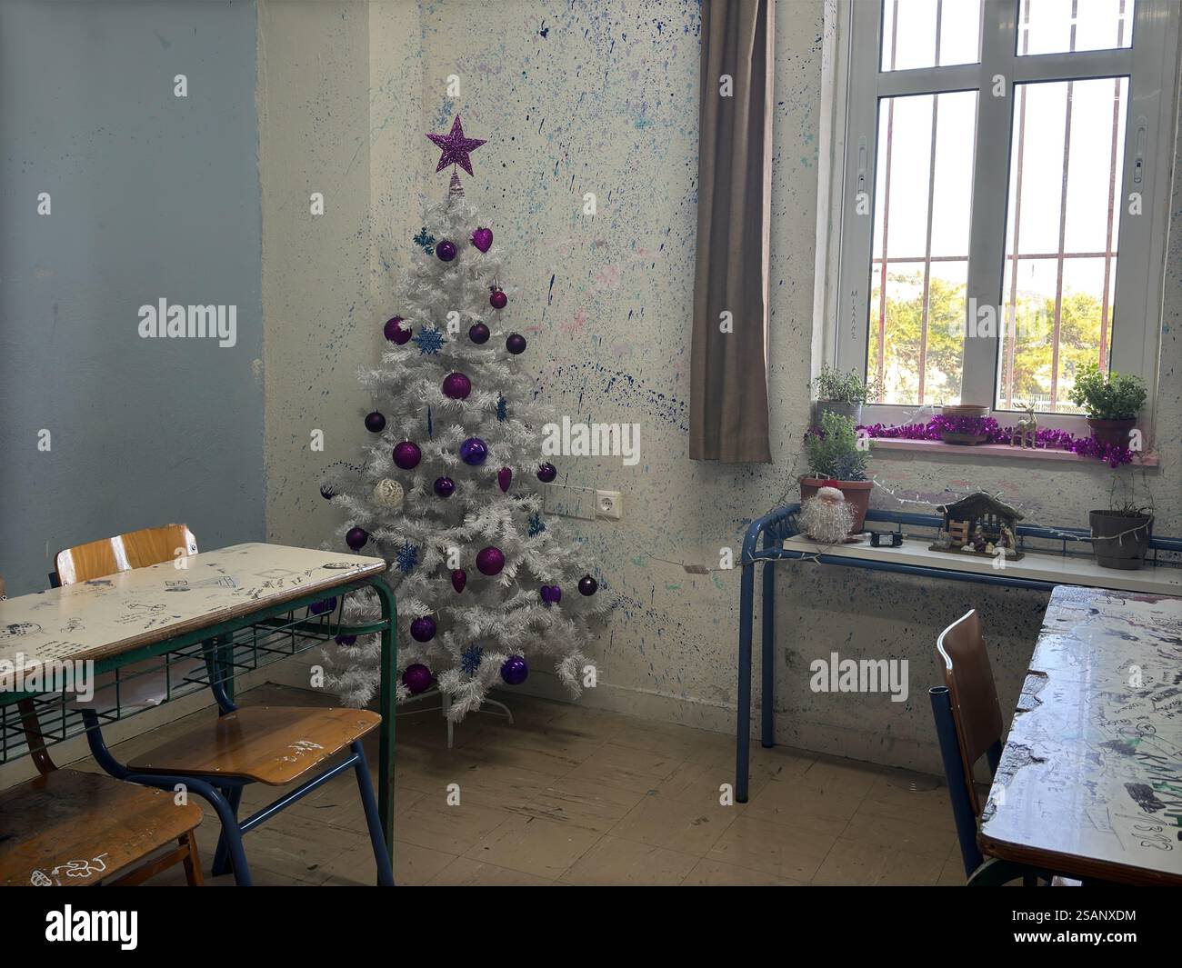 Un albero di natale con ornamenti, una stella in cima in un'aula scolastica - Una scrivania sotto la finestra con un Babbo natale acceso, una mangiatoia e luci natalizie Foto Stock