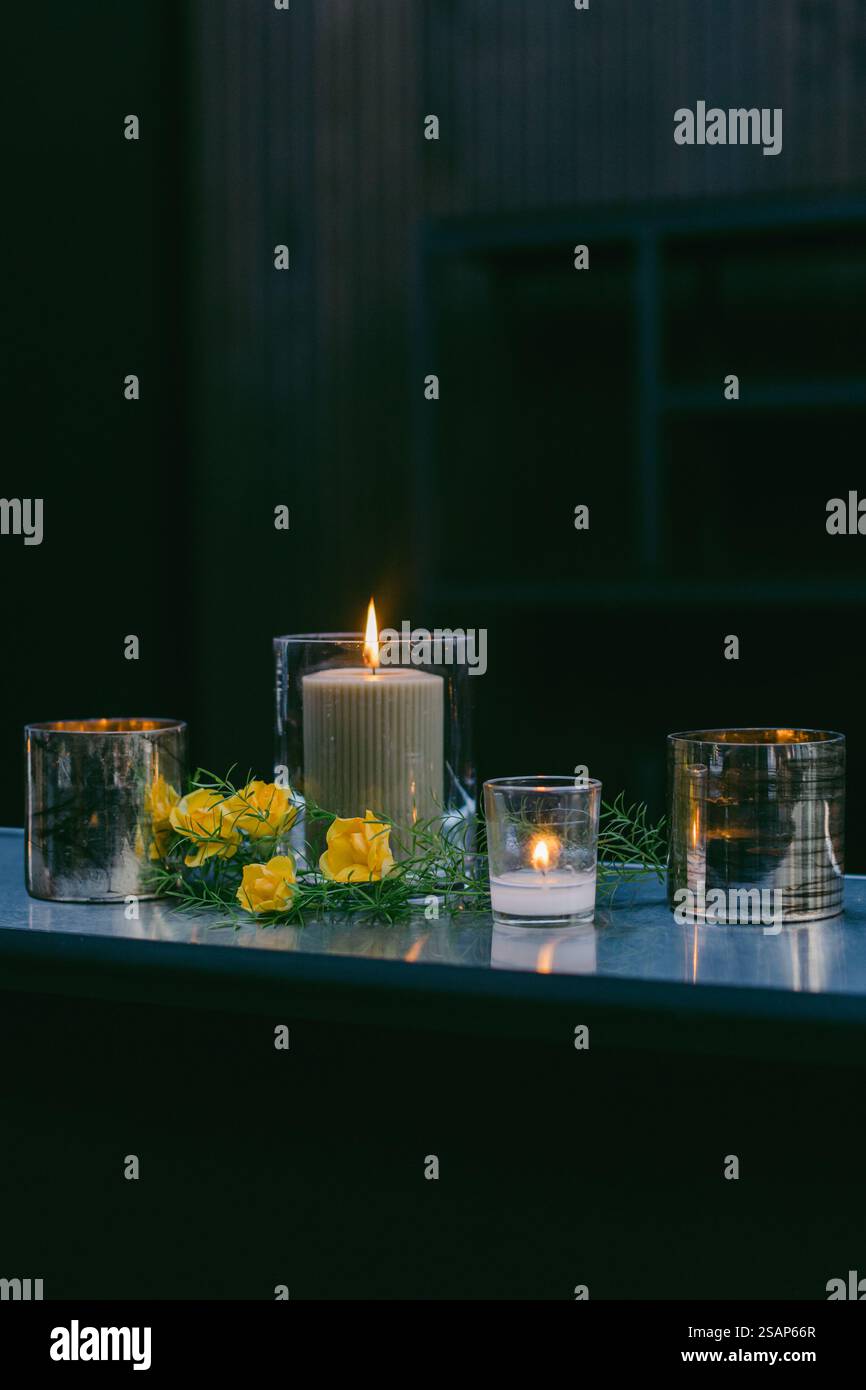 Una calda ed invitante esposizione presenta varie candele, tra cui una alta nel centro, circondata da vegetazione lussureggiante e fiori gialli luminosi, creat Foto Stock