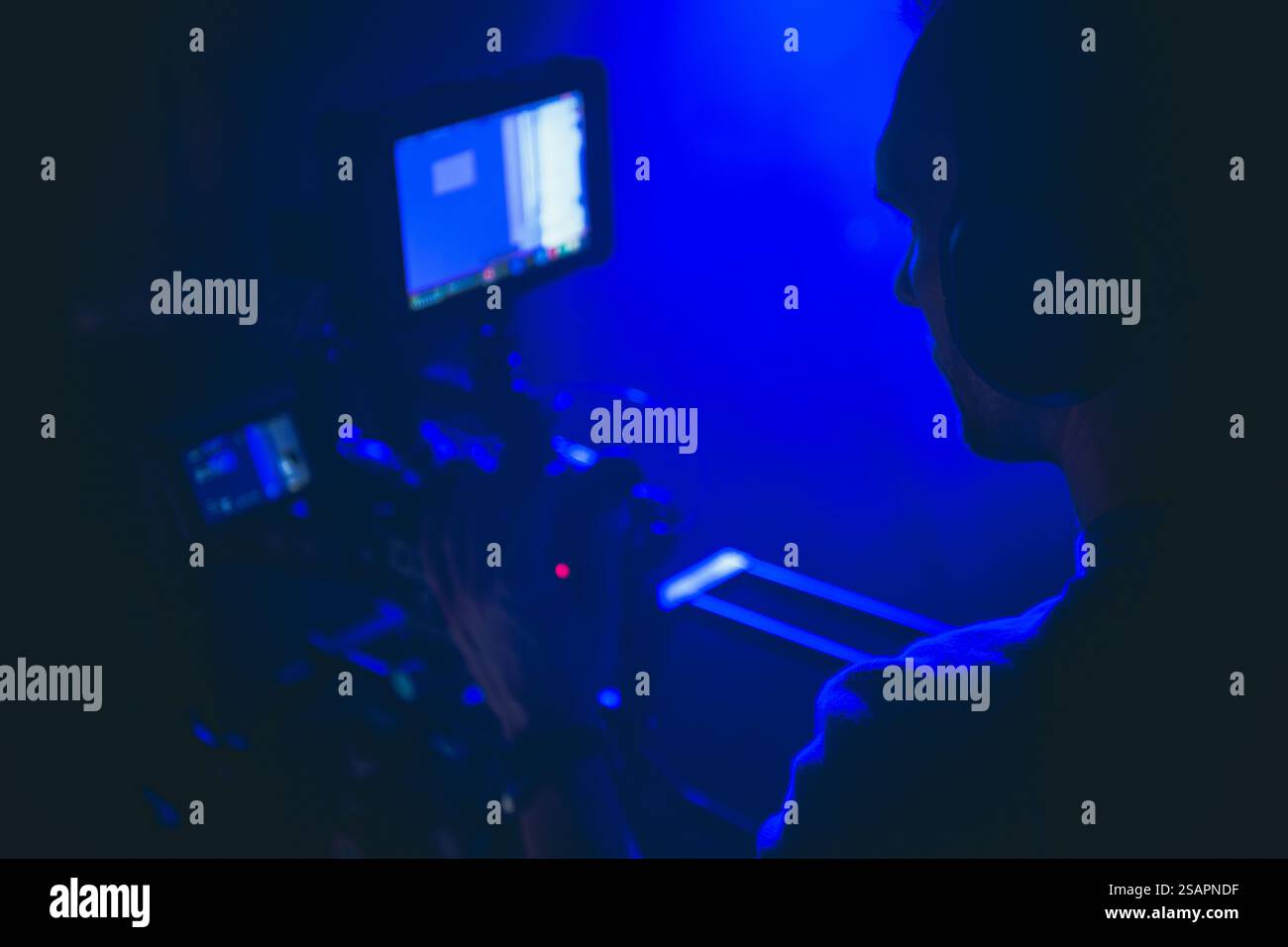 L'operatore di una telecamera regola le proprie apparecchiature con una luce blu soffusa, concentrandosi sull'acquisizione di filmati in un ambiente di produzione creativo di notte. Foto Stock