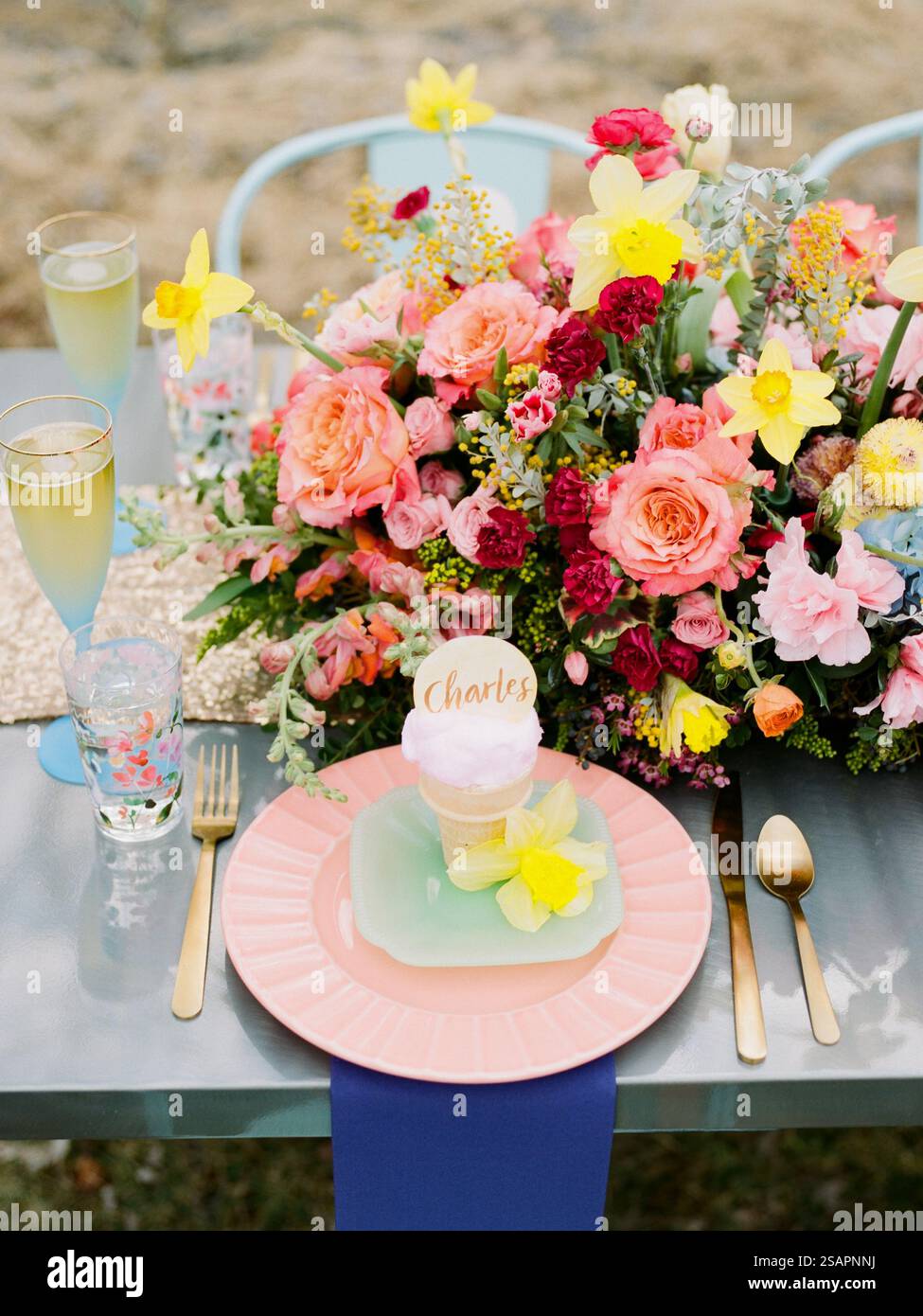Un tavolo all'aperto splendidamente allestito presenta un piatto pastello con un dessert personalizzato, fiori vivaci ed eleganti bicchieri, perfetto per una celebrità Foto Stock